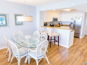 A modern kitchen with white cabinetry, a stainless steel refrigerator, and a glass dining table with wicker chairs.