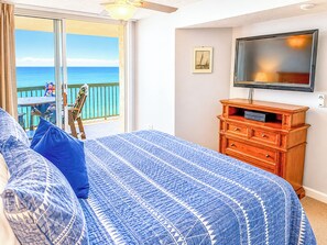 Ein Schlafzimmer mit einem Bett, einer Kommode, einem Fernseher, einem Fenster mit Meerblick und einem Deckenventilator.