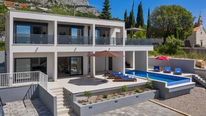 A modern two-story house with a swimming pool, outdoor seating, and a view of a mountain. - Modern holiday home with infinity pool, three bedrooms, terrace, sea view (Bast)