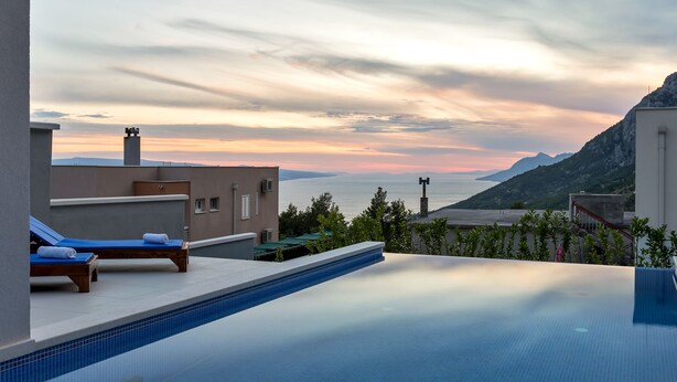 An infinity pool with lounge chairs, a view of the sea, and a mountainous landscape. - Modern holiday home with infinity pool, three bedrooms, terrace, sea view (Bast)