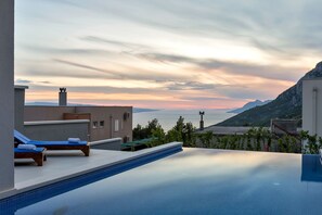 Una piscina infinita con sillones de descanso, vista al mar y un paisaje montañoso.
