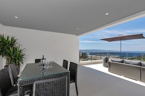 A modern dining area with a glass table, wicker chairs, and a view of the sea. - Modern holiday home with infinity pool, three bedrooms, terrace, sea view (Bast)