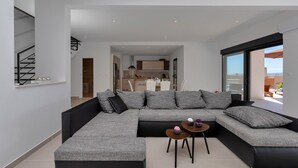 A modern living room with a sectional sofa, a small coffee table, and a view to the kitchen and balcony. - Modern holiday home with infinity pool, three bedrooms, terrace, sea view (Bast)
