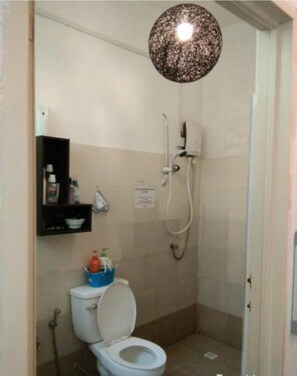 A small bathroom with a toilet, a shower, and a shelf with toiletries. - CoLiving Saga - Hostel (Bandar Seri Begawan)