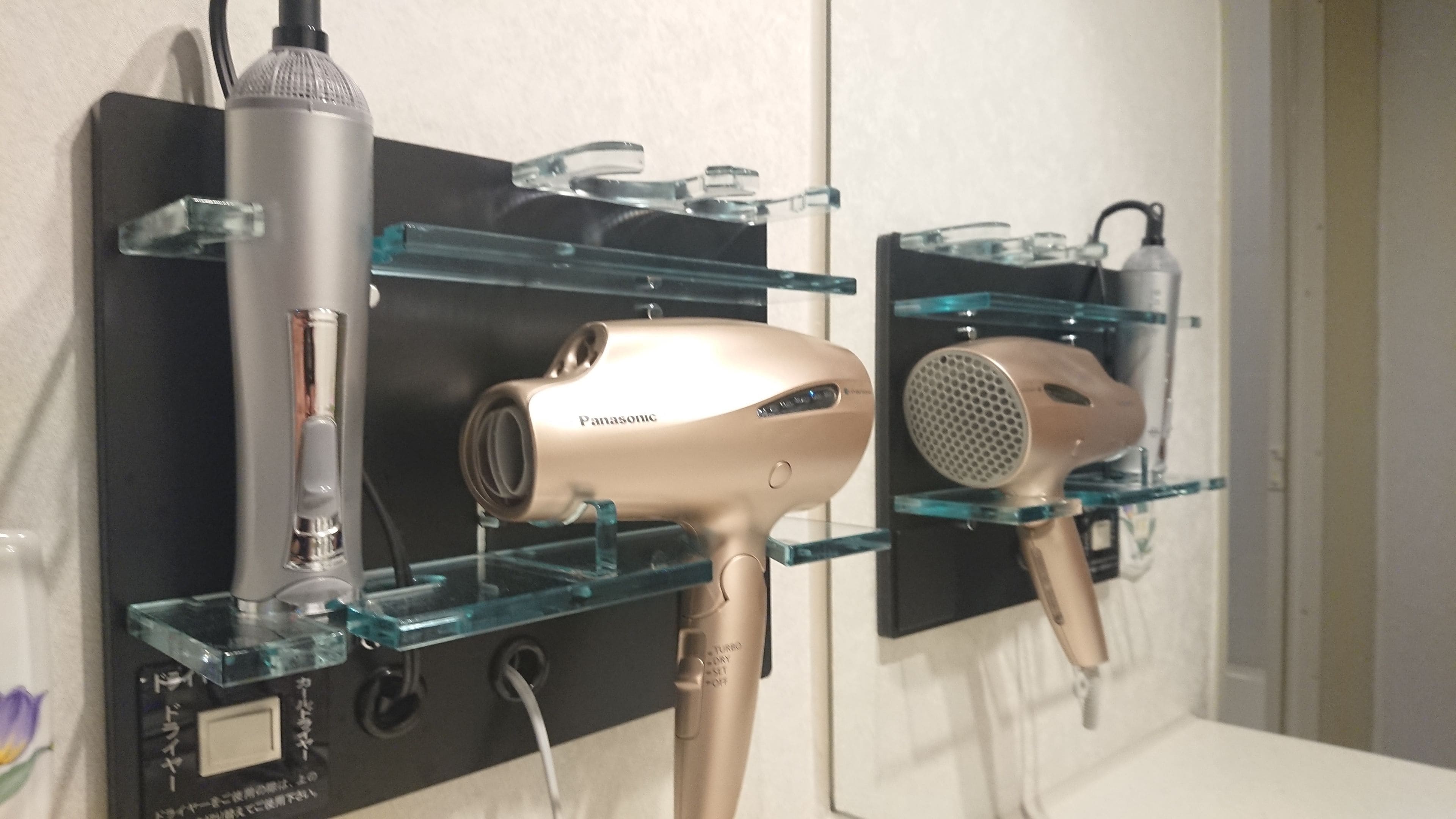 A hairdryer and a vacuum cleaner on a black shelf with glass shelves.