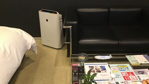 A hotel room with a bed, a black leather sofa, a glass coffee table with various items including remote controls, a small plant, and informational brochures. - Valentine - Adults Only (Tottori)