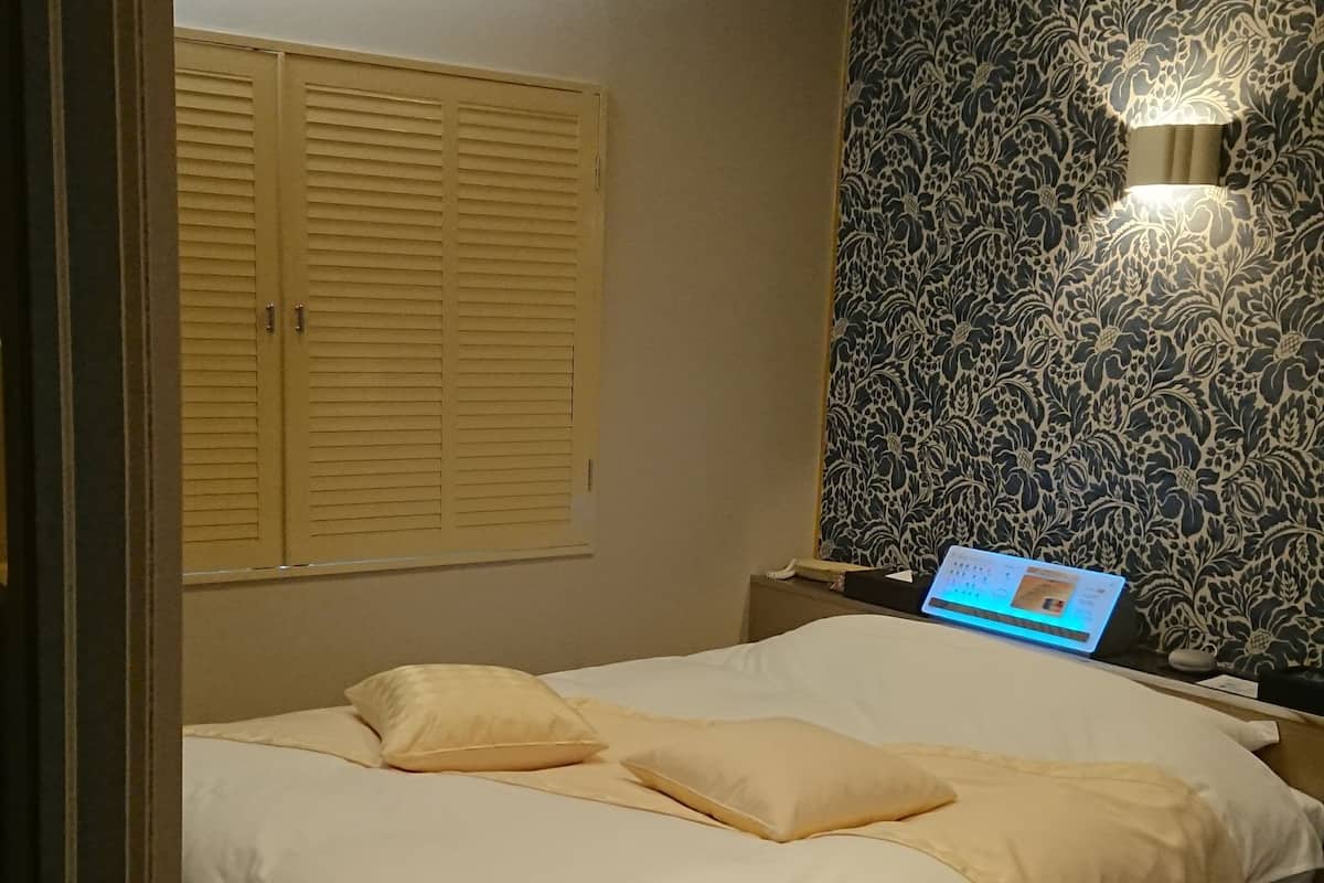 A bedroom with a bed, wooden floor, a wall-mounted light, and a patterned wallpaper.