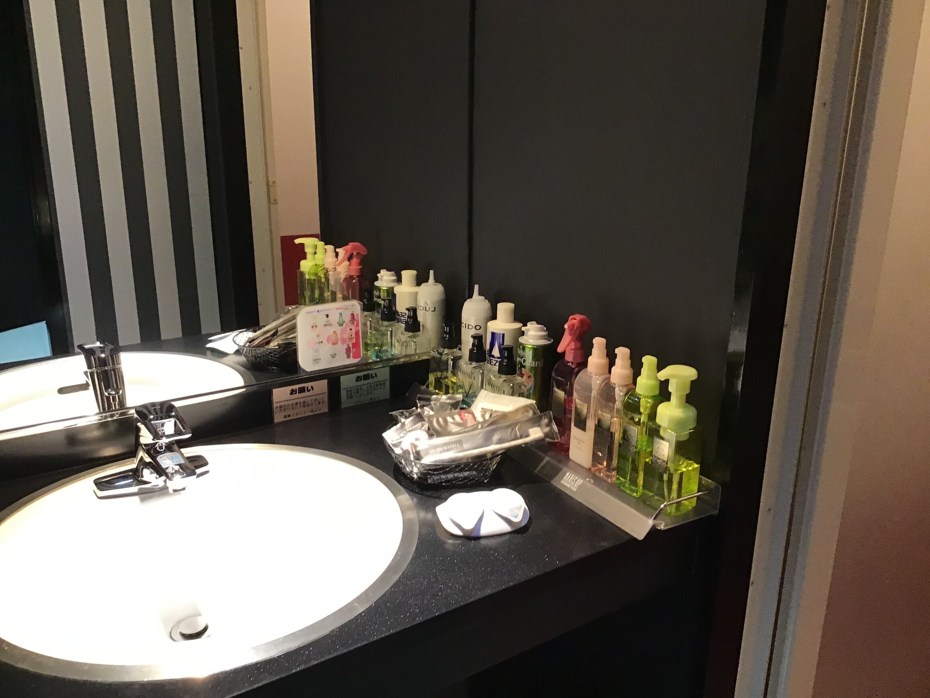 Baño con lavamanos, espejo y distintos artículos de aseo.