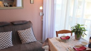 Un salon chaleureux avec un canapé, une table à manger dressée pour deux personnes et une plante en pot posée sur la table.