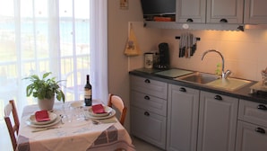 Une cuisine comprenant un coin repas, un évier, des placards, une horloge et une fenêtre donnant sur un paysage agréable.