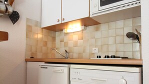 A compact kitchen with a dishwasher and a built-in oven, a light fixture above the counter, and a wall-mounted exhaust hood.