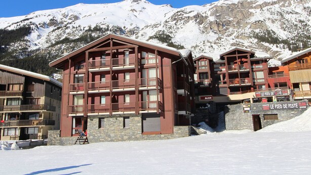 A multi-story wooden building with balconies, likely a hotel, with a snowy mountain backdrop.