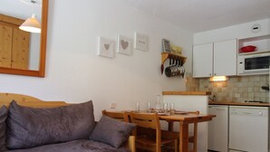 A compact living space with a sofa, dining table, chairs, a kitchen area with cabinets, a microwave, and a dishwasher.