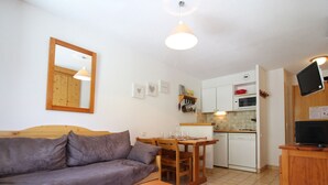 A compact living space with a sofa, a wooden table, a kitchen area with a microwave, and a television.