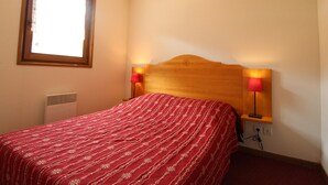 Un dormitorio con cabecera de madera, colcha roja, dos lámparas de noche, una ventana y un calentador de pared.