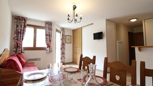 Un comedor con una mesa preparada para cuatro, una araña y un televisor montado en la pared.