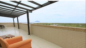 Un espace extérieur abrité, offrant une vue sur un paysage lointain, doté d’un sol carrelé et de deux canapés orange.