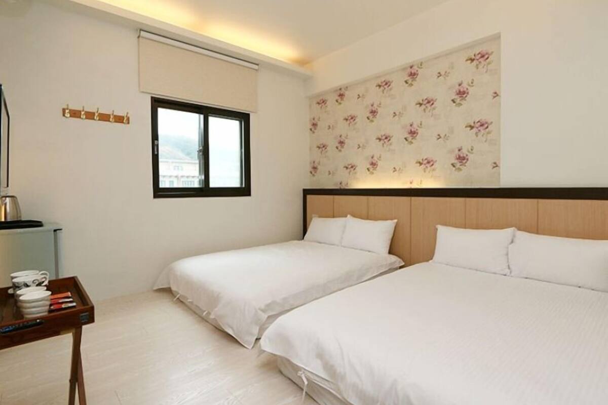 Een hotelkamer met twee bedden, een klein tafeltje met een dienblad en diverse voorwerpen, een raam en bloemenbehang.