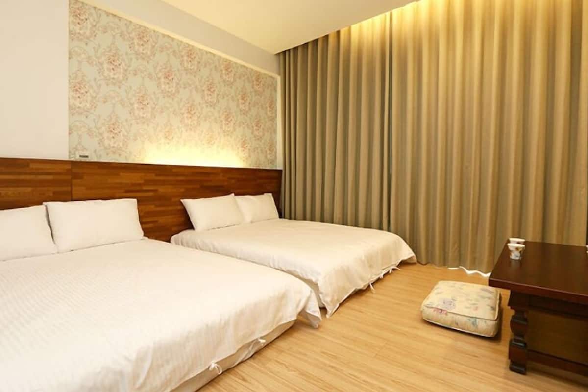 Een hotelkamer met twee bedden, een houten hoofdeinde, een bloemendecoratie aan de muur en een gordijn.
