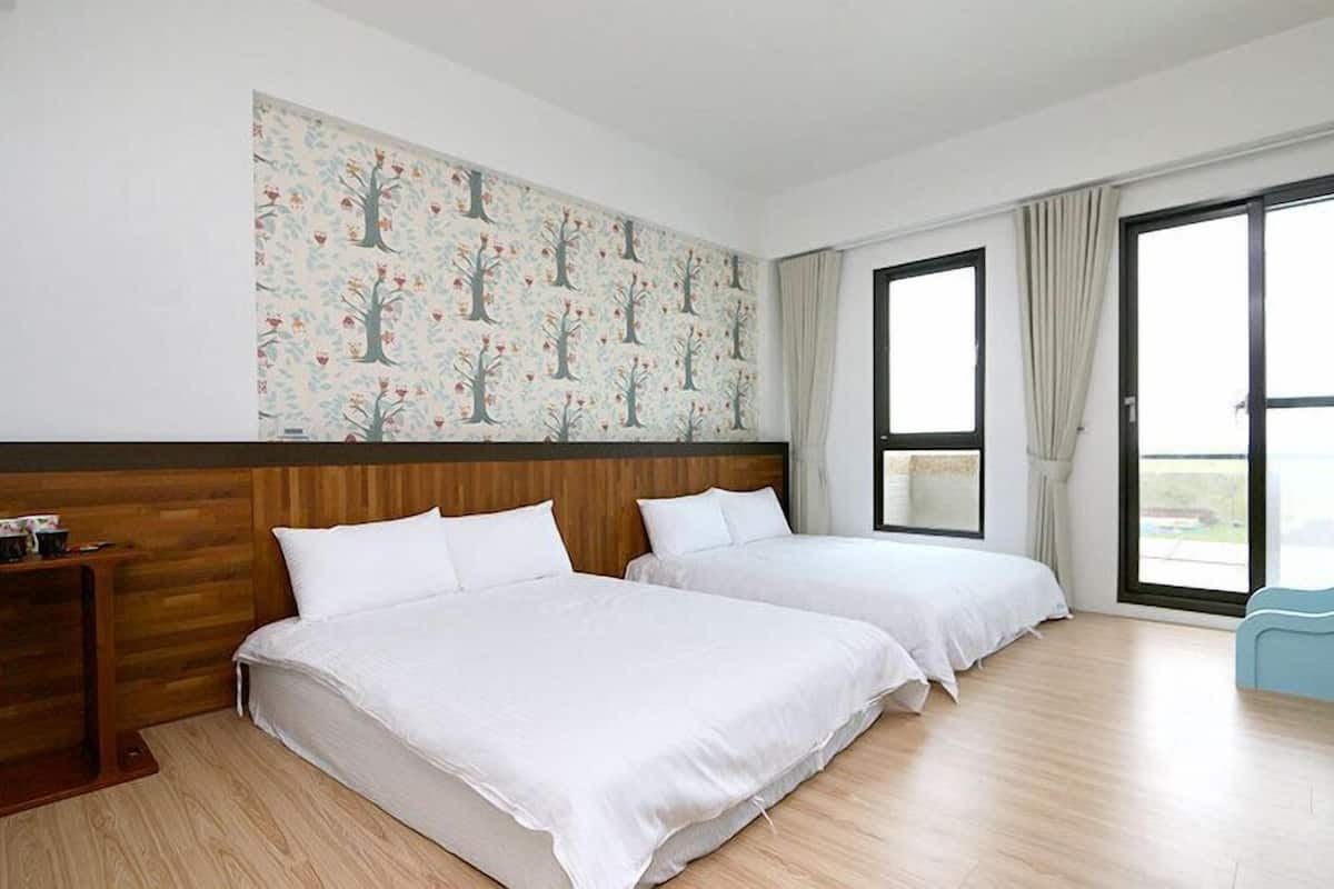 Een hotelkamer met twee bedden, een houten hoofdbord, een groot raam en een muur met een boommotief.