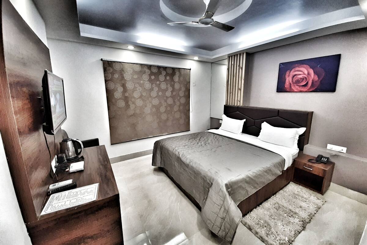 A modern bedroom with a bed, bedside tables, a desk with a computer, a ceiling fan, and a large window with curtains.