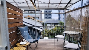 A wooden deck with a metal railing, a blue chair, a round table with a white cushion, and a white chair. - RYOKAN PLUM (Odawara)