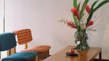 Een eetruimte met een houten tafel, blauw-rode gestreepte stoelen, een decoratieve vaas met bloemen en een hanglamp.
