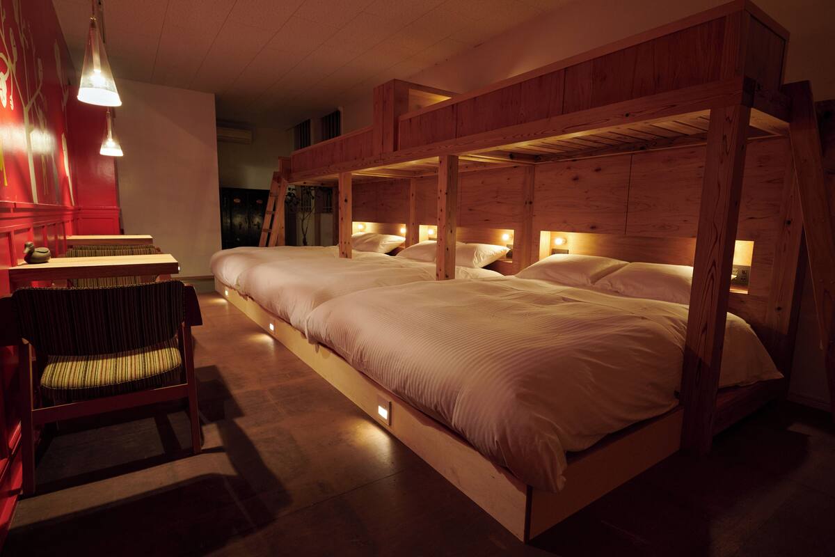 Een kamer met een stapelbed, een stoel en een tafel met een lamp.