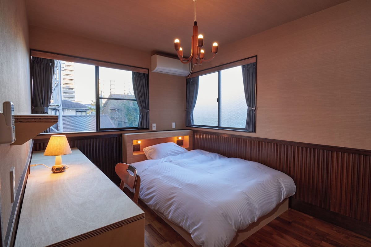 Een slaapkamer met een bed, nachtkastje, lamp en grote ramen.