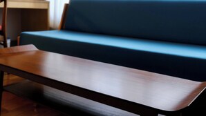 A wooden table in a room with a blue sofa and a window with curtains. - RYOKAN PLUM (Odawara)