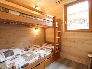 Une chambre dans un chalet en bois, avec des lits superposés, une fenêtre et une couvre-lit matelassé.