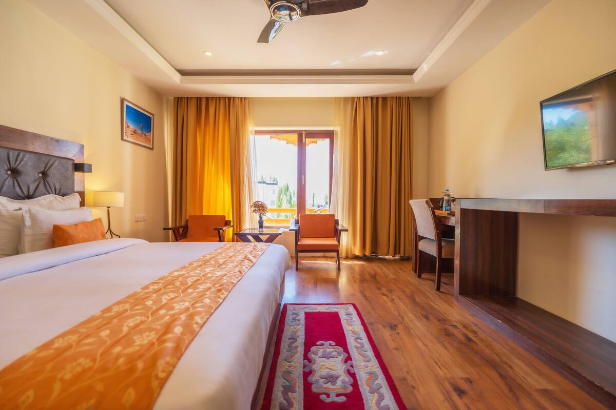A hotel room with a large bed, a desk, a chair, a television, and a view of the outdoors.