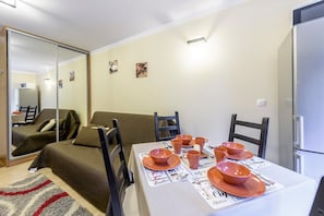 A compact living space with a dining area set for four, a sofa, and a refrigerator.