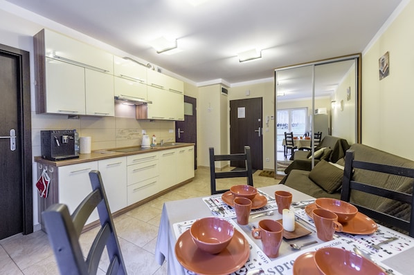 A modern kitchen with white cabinets, a dining table set with orange dishes, and a dark wooden chair.