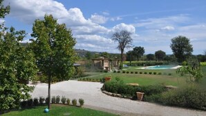 Un jardí ben cuidat amb un camí de grava que condueix a un edifici, una piscina i un cel blau clar.