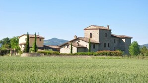 Un edifici de pedra amb una torre, envoltat per un camp i arbres.