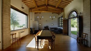Una habitació espaiosa amb una llarga taula de fusta i caires, grans finestres i un sostre volta.