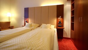 A hotel room with two beds, a nightstand, a lamp, and a wardrobe. - Hotel Hanken (Wangerooge)