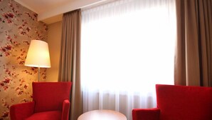 A hotel room with two red armchairs, a small round table, a floor lamp, and a window with sheer curtains. - Hotel Hanken (Wangerooge)