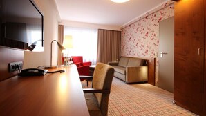 A hotel room with a wooden desk, a television, a sofa, and a patterned carpet. - Hotel Hanken (Wangerooge)