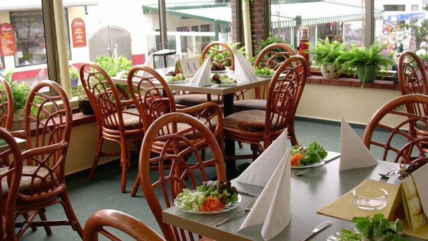 An indoor dining area with wicker chairs and tables, some with menus and water glasses. - Hotel Hanken (Wangerooge)
