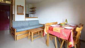 Un coin repas avec une table en bois dressée pour quatre personnes, un banc et, au fond, un espace cuisine.