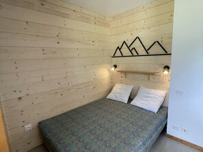 A room with wooden walls, a bed with patterned bedding, two white pillows, and a wall-mounted light fixture.
