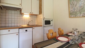 A compact kitchen with white cabinets, a Bosch dishwasher, a microwave, and a dining area with a striped tablecloth and wooden chairs. - Cozy apartment for 4 with WIFI and parking in Lanslevillard (Lanslevillard)
