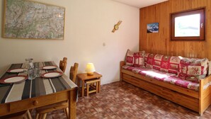 A cozy room with a wooden dining table set for four, a wooden bench with patterned cushions, a map on the wall, and a window with a view. - Cozy apartment for 4 with WIFI and parking in Lanslevillard (Lanslevillard)