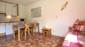 A compact kitchen with a dining area, a small table with chairs, a wall clock, and a patterned sofa. - Cozy apartment for 4 with WIFI and parking in Lanslevillard (Lanslevillard)