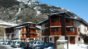 A hotel with multiple balconies, a parking lot with several cars, and a sign indicating camping facilities. - Cozy apartment for 4 with WIFI and parking in Lanslevillard (Lanslevillard)