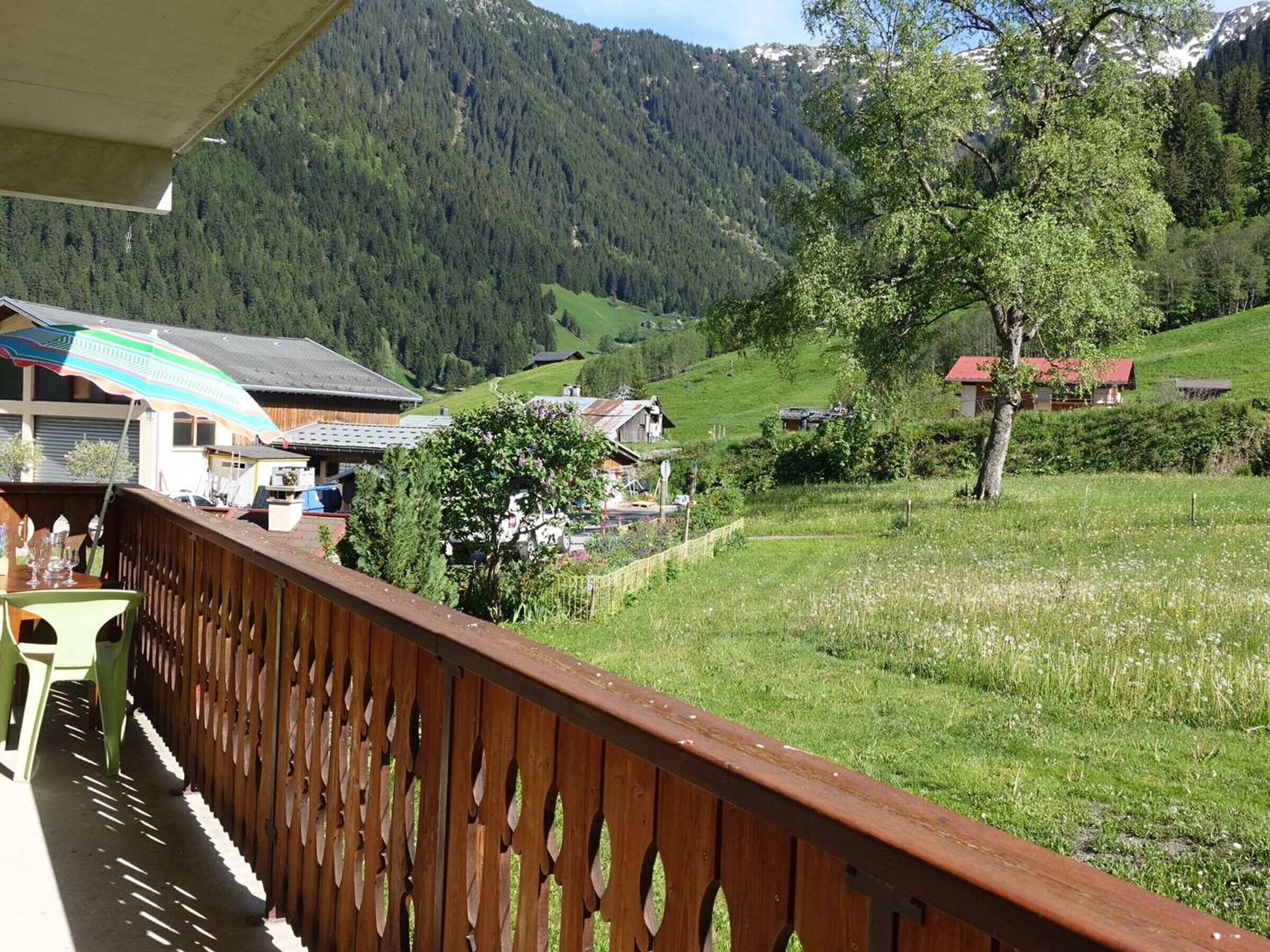 Un balcon doté d’une balustrade en bois, donnant sur un paysage verdoyant avec des maisons et une montagne.