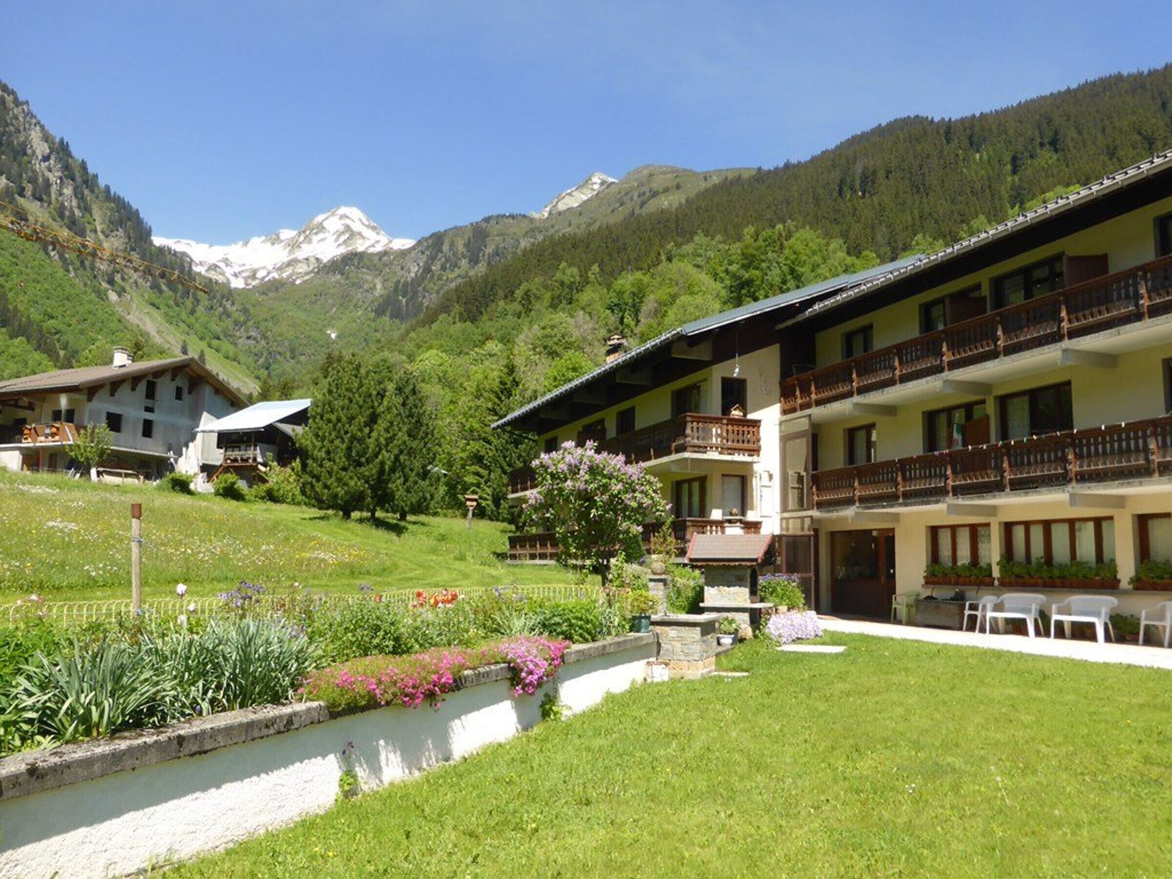 A hotel with a mountain backdrop, featuring a well-maintained garden, outdoor seating, and a traditional architectural style.