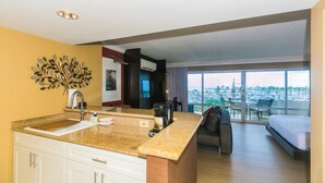 Quarto de hotel com cozinha, cama e varanda com vista para o porto de iates.